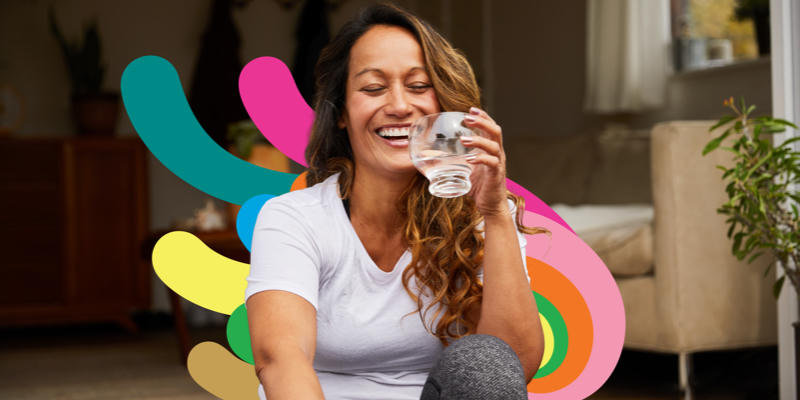 Woman sitting outside laughing while holding a glass of water