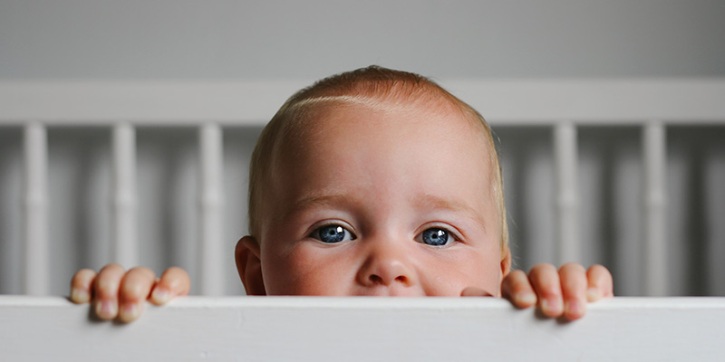 An awake baby looking over the bars of their cot